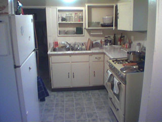 looking into my kitchen, formica on floor, fridge to left, range to right, cabinets and sink ahead
