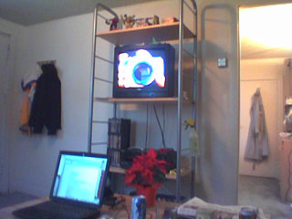 coffee table in the foreground with laptop and poinsetta on it, tv on a shelf unit, coats on coathooks, and an entrance into another room
