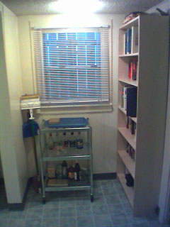 A bookcase, metal cart and mop in a corner