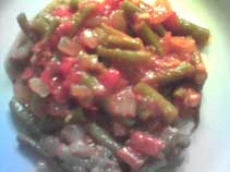 a plate of cooked green beans with red tomatoes